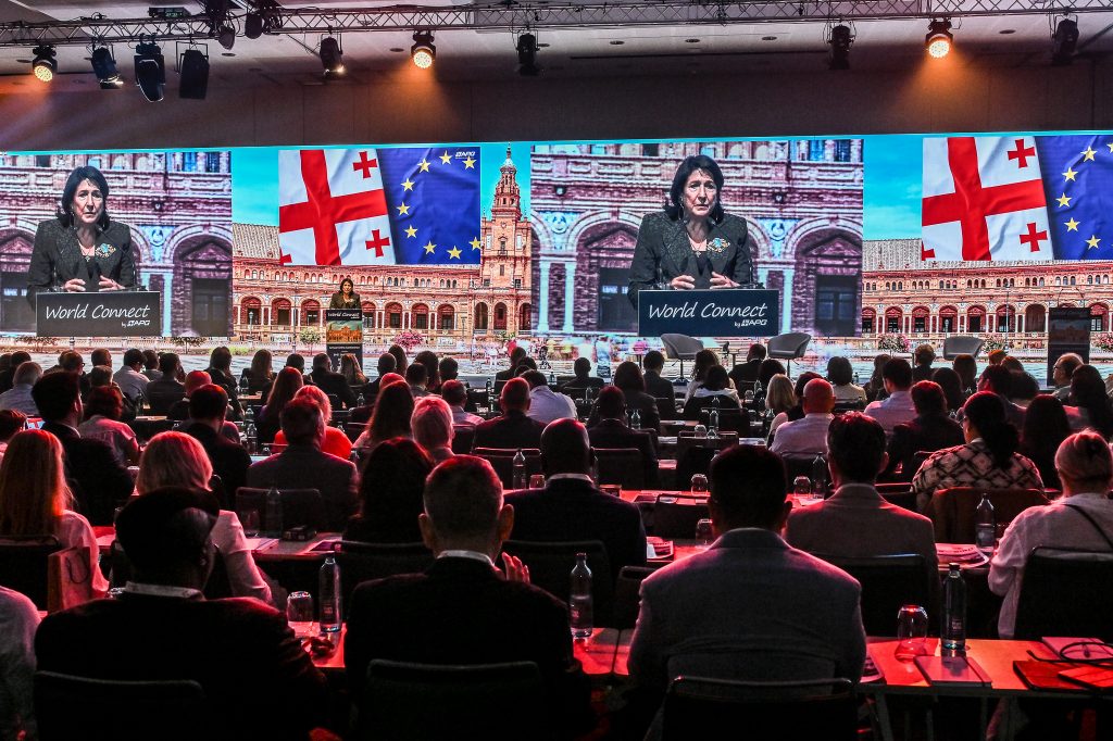 Photo reportage d’une conférence internationale, prise depuis la salle, avec une intervenante politique à la tribune.